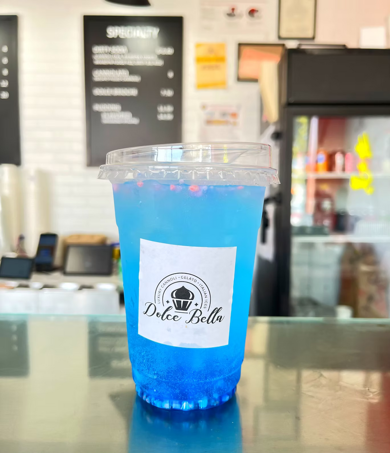 Blue drink in a plastic cup with a 'Dolce Bella' label, blurred cafe interior in the background