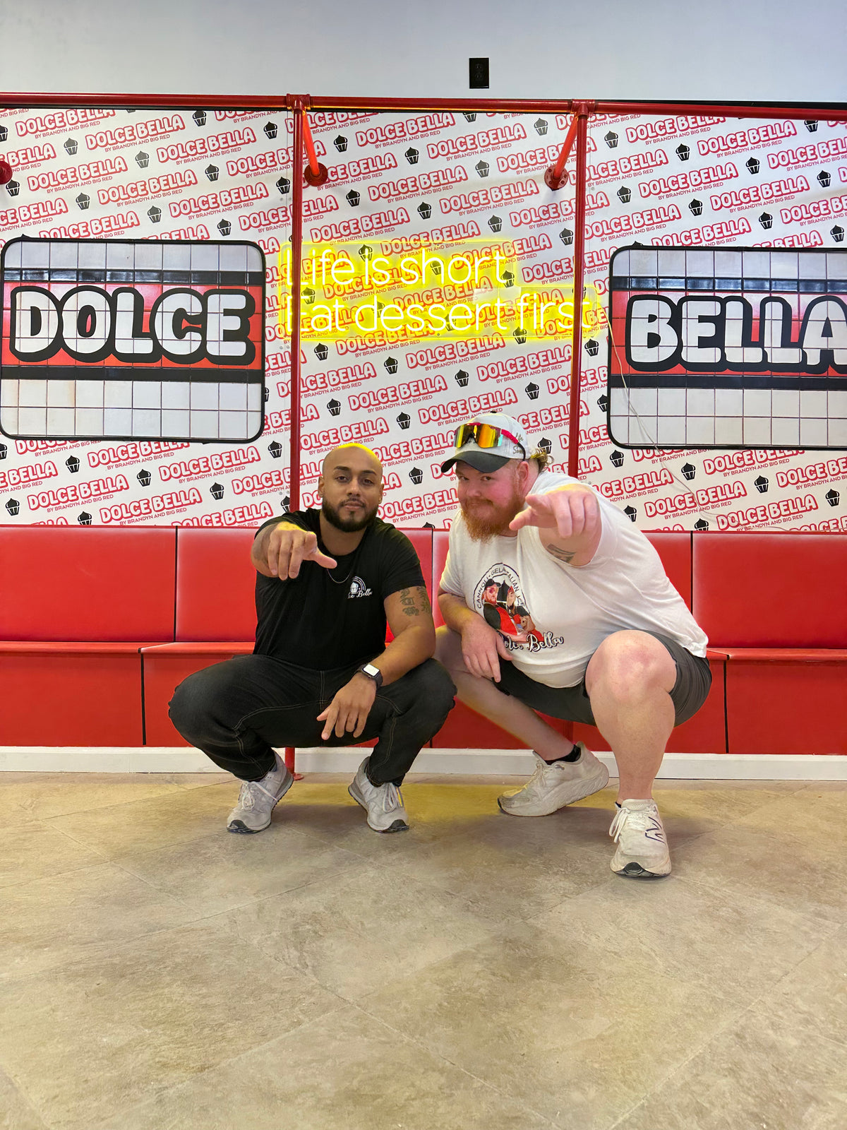 Two men posing in front of a branded dolce bella wall.